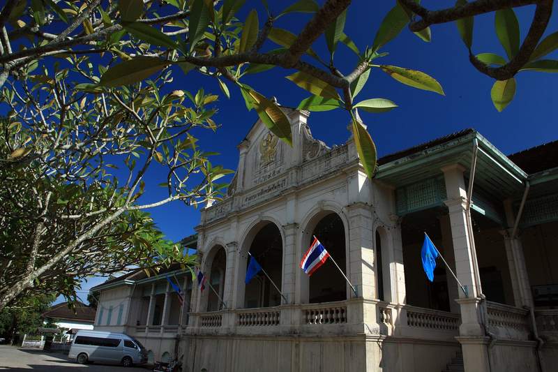 อาคารเก่าสีขาวแบบตะวันตกใต้กิ่งไม้และท้องฟ้าสีคราม